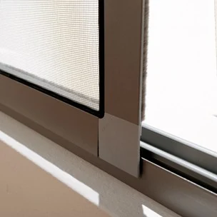 Detalle de la malla de una mosquitera junto al marco de una ventana.